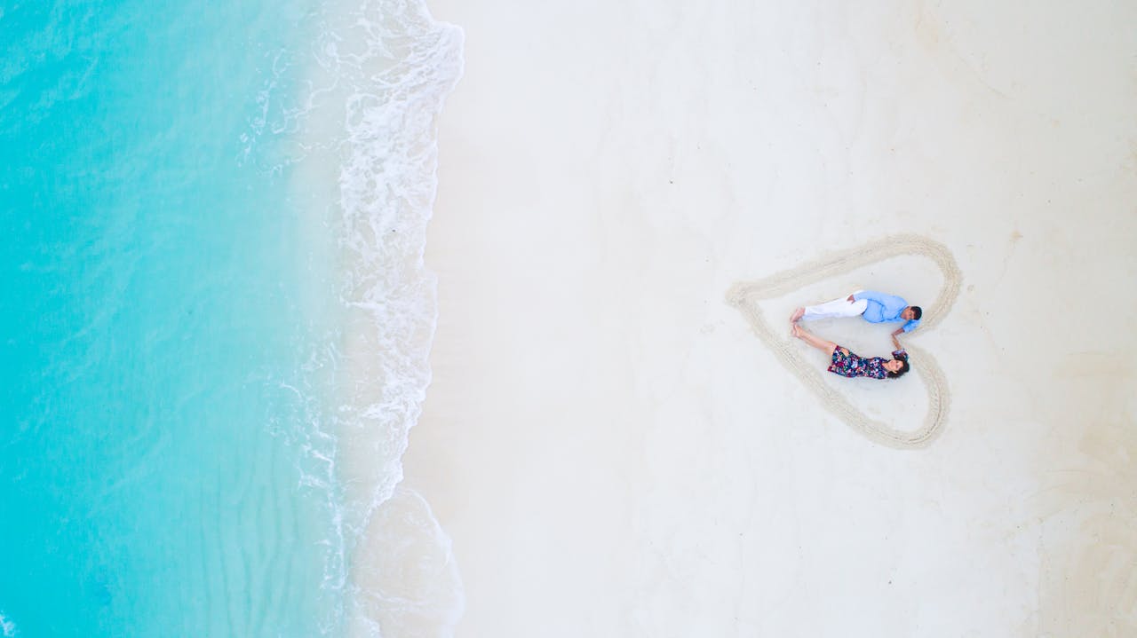 Aerial view of a couple lying on a beach in the Maldives, framed in a heart shape in the sand.